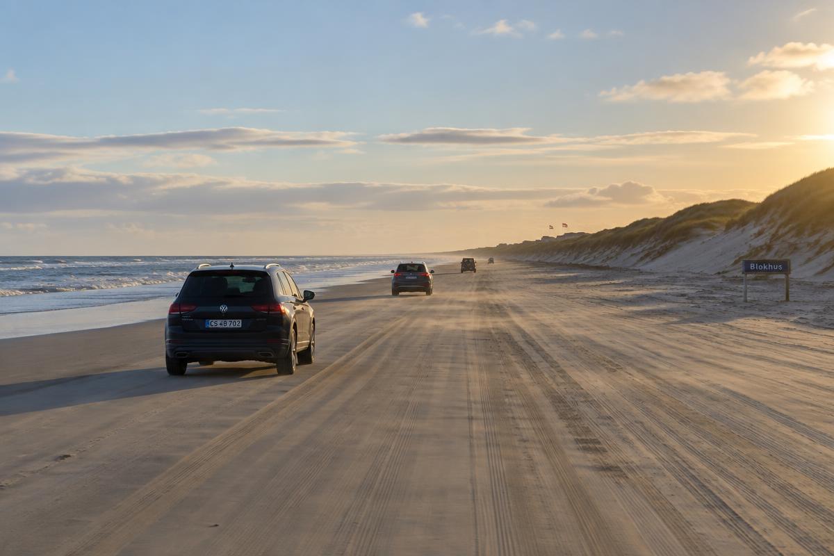 Auto's rijden over het harde zandstrand bij Blokhus met duinen langs de kust