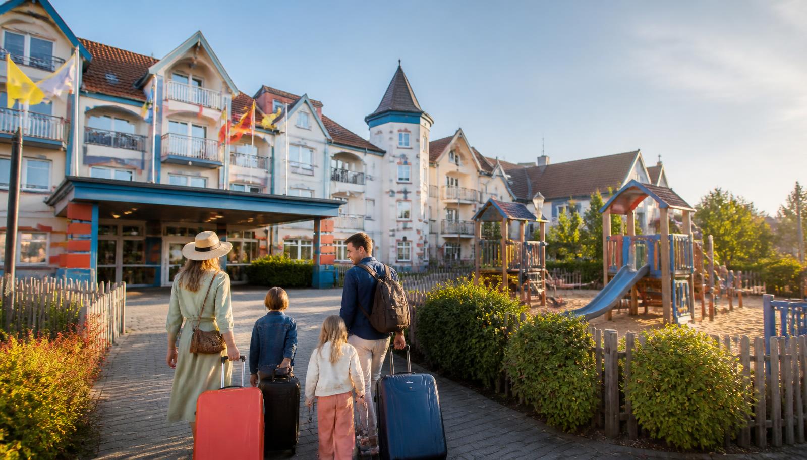 Kleurrijk themahotel met speeltuin en aankomend gezin met koffers vlak bij een pretpark aan de Belgische kust.