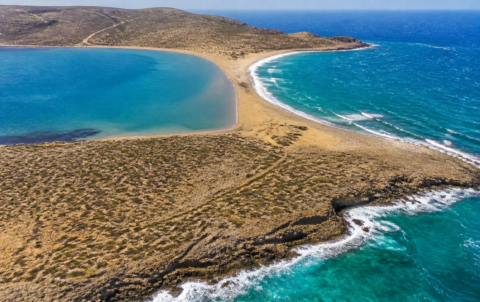 Luchtbeeld van de zandtong van Prasonisi aan de zuidpunt van Rhodos met kalm water aan de ene en golven aan de andere zijde.