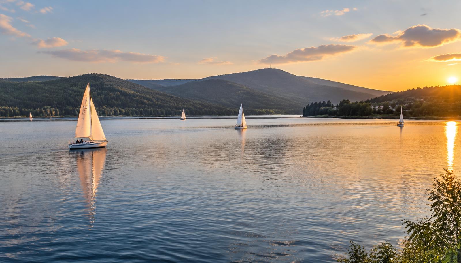 Zeilboten op het Lipnomeer bij zonsondergang met de beboste heuvels van het Šumava-gebergte